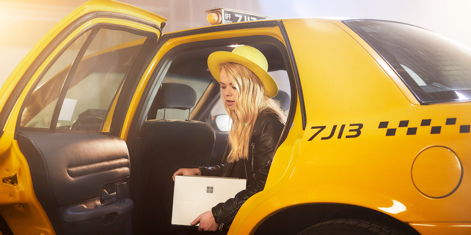 Woman with yellow hat stepping out of yellow cab with a Surface