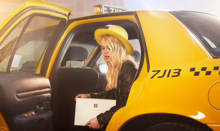 Woman with yellow hat stepping out of yellow cab with a Surface