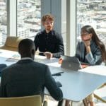 ryhmä ihmisiä, jotka istuvat pöydässä kannettavan tietokoneen avulla