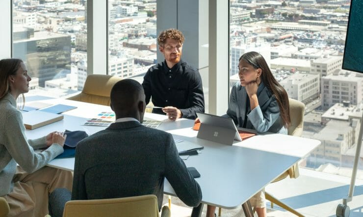 ryhmä ihmisiä, jotka istuvat pöydässä kannettavan tietokoneen avulla