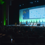 a crowd of people in a dark room listening to a presentation