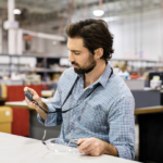 Male worker seated at desk using Askey IoT device in commercial manufacturing factory.