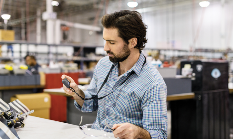 Male worker seated at desk using Askey IoT device in commercial manufacturing factory.
