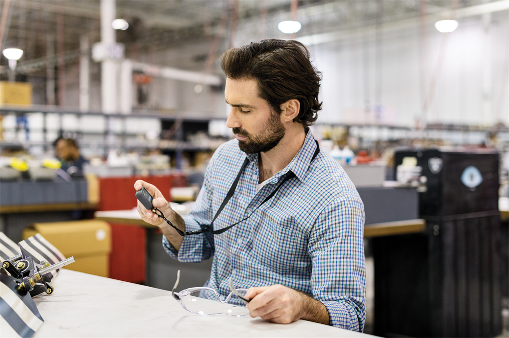 Male worker seated at desk using Askey IoT device in commercial manufacturing factory.