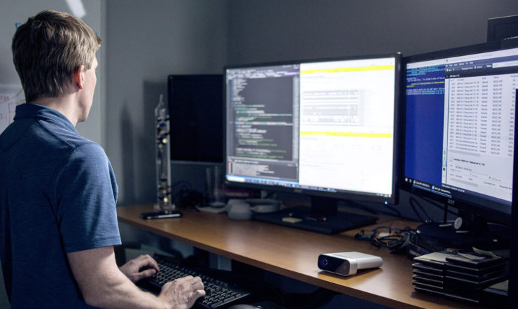 mies seisoo vieressä tietokoneen näytön pöydällä