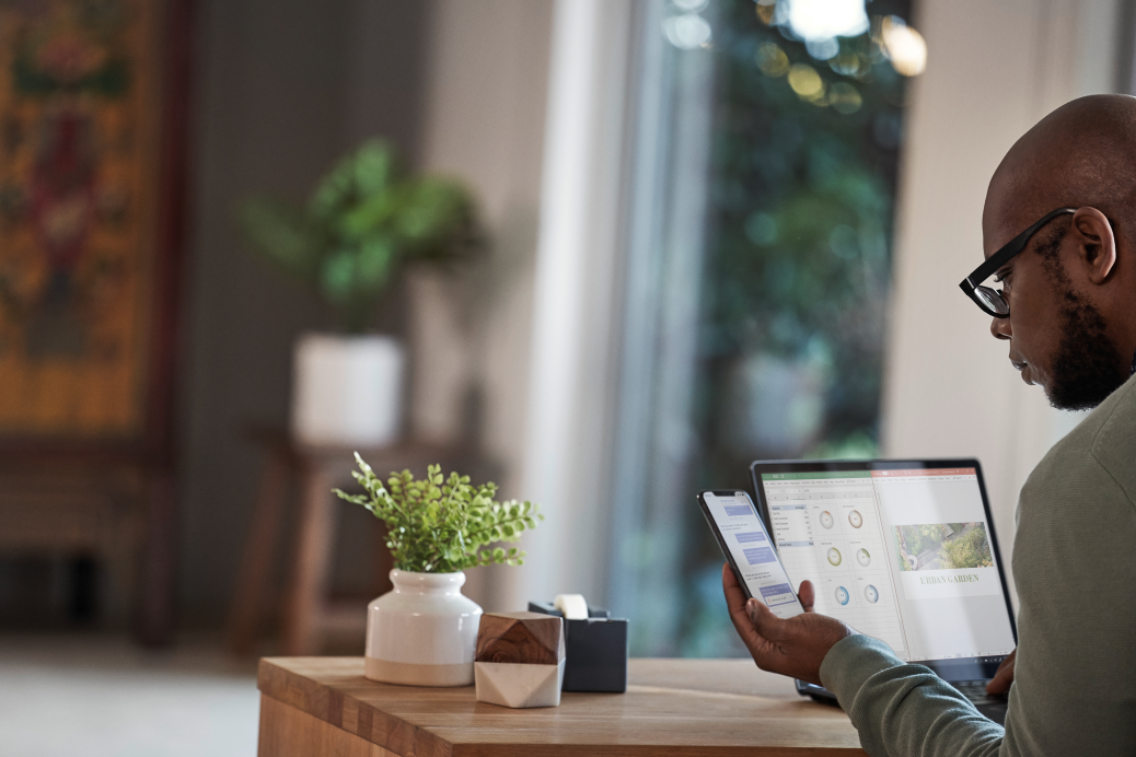 Male working remotely from his home office on a Dell Latitude 13 device, running Microsoft Excel and PowerPoint, checking phone.