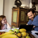 Father and daughter at dining room table on laptop; Photographer: Bobo Olsson