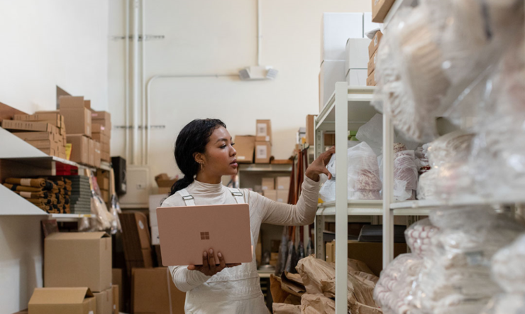 Contextual image of woman holding Surface Laptop 3 in Sandstone working in a warehouse.