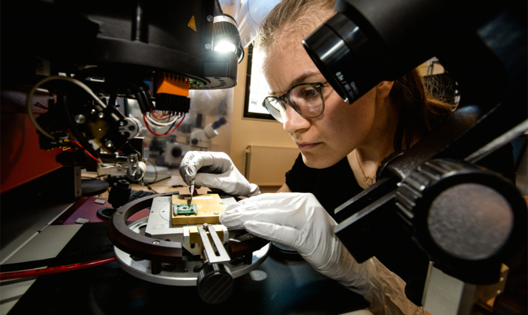 Female scientist wearing plastic gloves while examining a microchip in quantum technology lab.