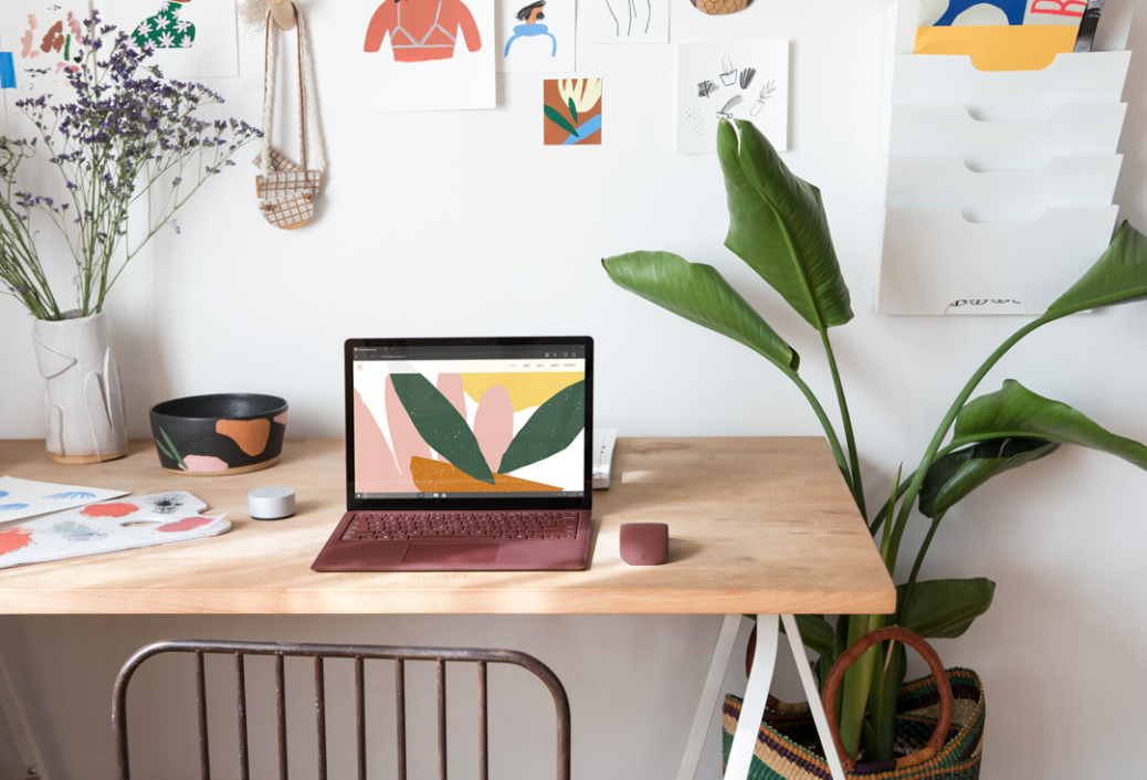een bureau met laptop en een vaas van bloemen op een lijst