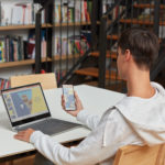 en mand ved hjælp af en bærbar computer sidder på toppen af en bog hylde