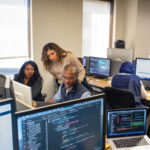 Two females, one mail behind computer screens