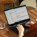 henkilö, joka käyttää kannettavaa tietokonetta ja istuu puupöydän päällä