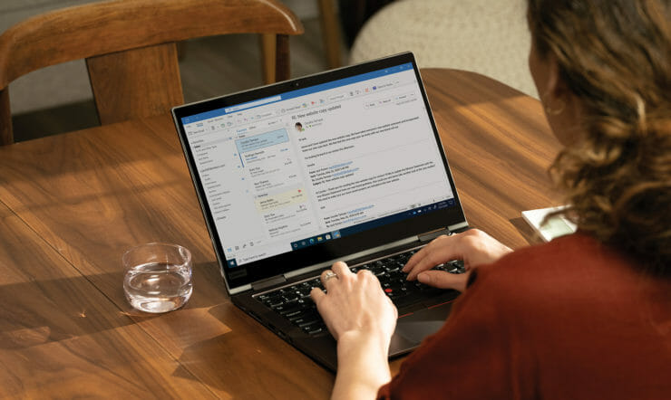 henkilö, joka käyttää kannettavaa tietokonetta ja istuu puupöydän päällä