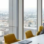 een persoon die bij een lijst met laptop voor een venster zit