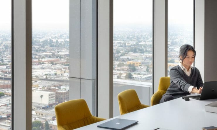 een persoon die bij een lijst met laptop voor een venster zit