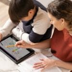 een jonge jongen die bij een lijst met behulp van een laptop zit