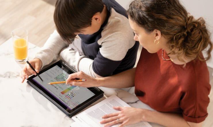 een jonge jongen die bij een lijst met behulp van een laptop zit