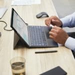 een mens die een laptopcomputer gebruikt die bovenop een houten lijst zit