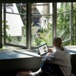 Nainen istuu tietokoneen ääressä ikkunan vieressä