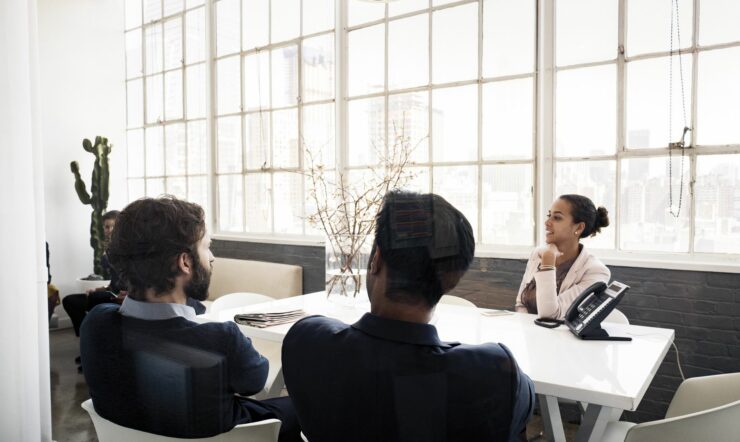 Two men and a woman sitting across the table and talking in a light room.