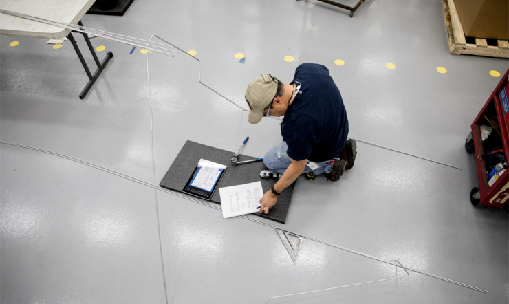 Overhead view of male worker kneeling on manufacturing factory floor and reaching for notes written on paper. An open tablet lays in front of him, with the Microsoft Azure dashboard shown.