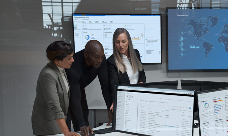 One man and two women in a boardroom looking at a screen with data