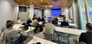 Ihmisiä istumassa pöytien ääressä työpajassa.